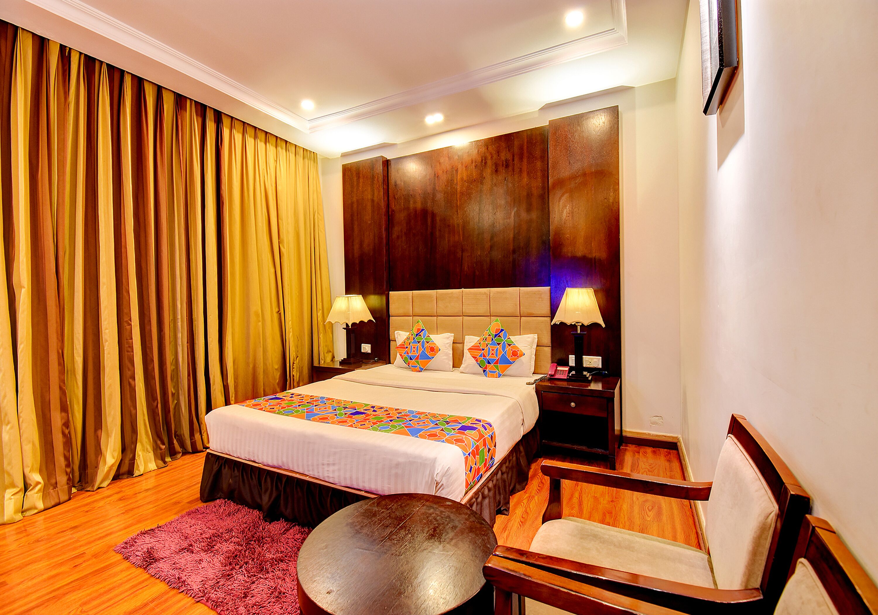 A hotel room with a large bed, two bedside tables with lamps, a wooden chair, and a round table.