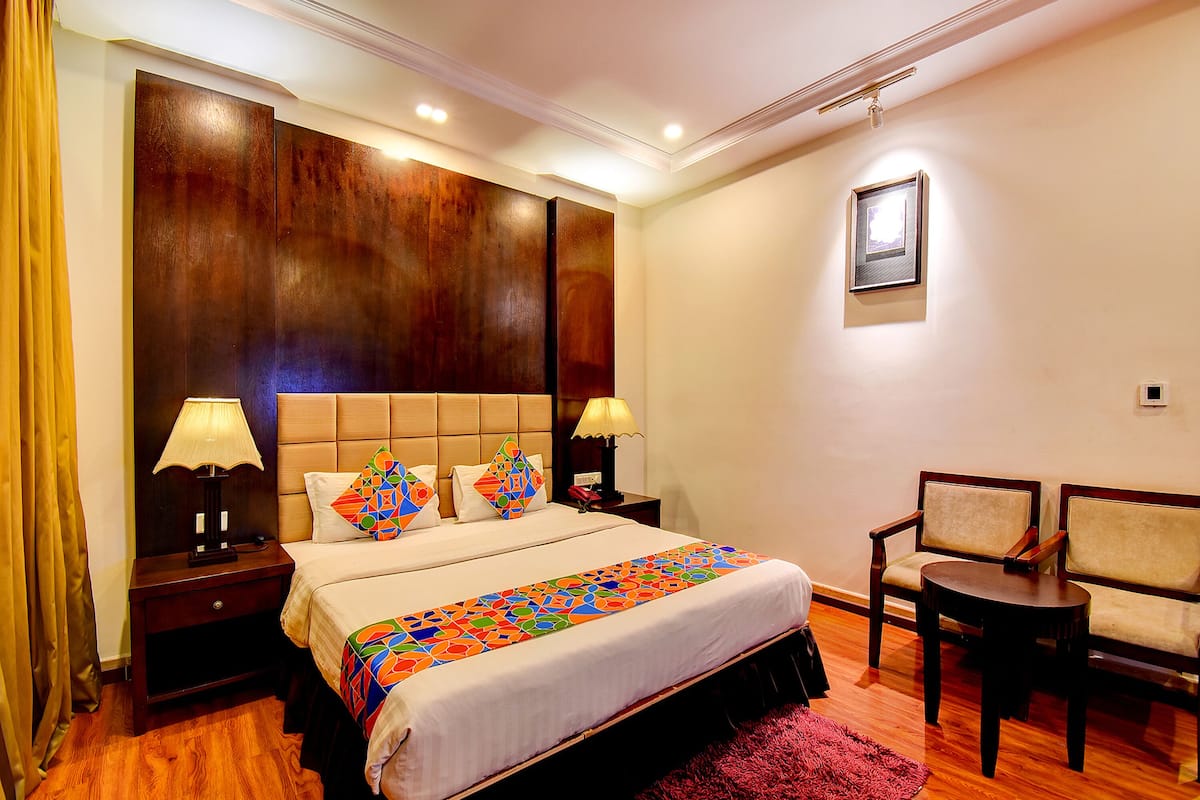 A hotel room with a large bed, two bedside tables with lamps, a small round table, two chairs, and a wooden headboard.