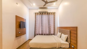 A neatly arranged bedroom with a bed, a mounted TV, and a ceiling fan. - Fabexpress Global Inn New (Lucknow)