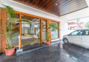 Enter a stylish hotel with a beautifully landscaped entrance, featuring glass doors and a welcoming atmosphere.