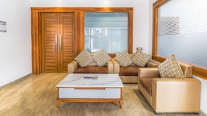 A modern living room with a sofa set, a coffee table, and a large window with blinds. - Fabexpress Global Inn New (Lucknow)