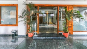 A hotel entrance with a glass door, potted plants, and a trash bin. - Fabexpress Global Inn New (Lucknow)