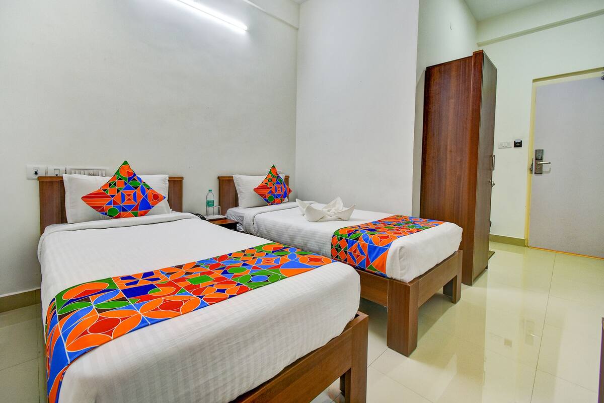 Una habitación de hotel con dos camas, cada una con una colcha y almohadas a juego con llamativos diseños geométricos. La habitación tiene un armario de madera y una puerta blanca.