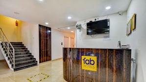 Zona de recepción de un hotel con un mostrador de madera, un televisor de pantalla plana y una escalera.