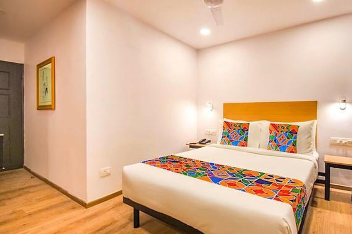Una habitació d'hotel amb un llit, una taula de nit, una làmpada penjada a la paret i una porta.