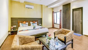 A hotel room with a bed, two armchairs, a glass coffee table, a ceiling fan, and a window with curtains. - FabHotel The Gayatri Palace (Lucknow)