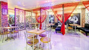 A restaurant with tables and chairs, decorative screens, and artwork on the walls. - FabHotel The Gayatri Palace (Lucknow)