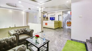 A hotel lobby with leather sofas, a glass coffee table, a reception desk, and a green carpet. - FabHotel The Gayatri Palace (Lucknow)