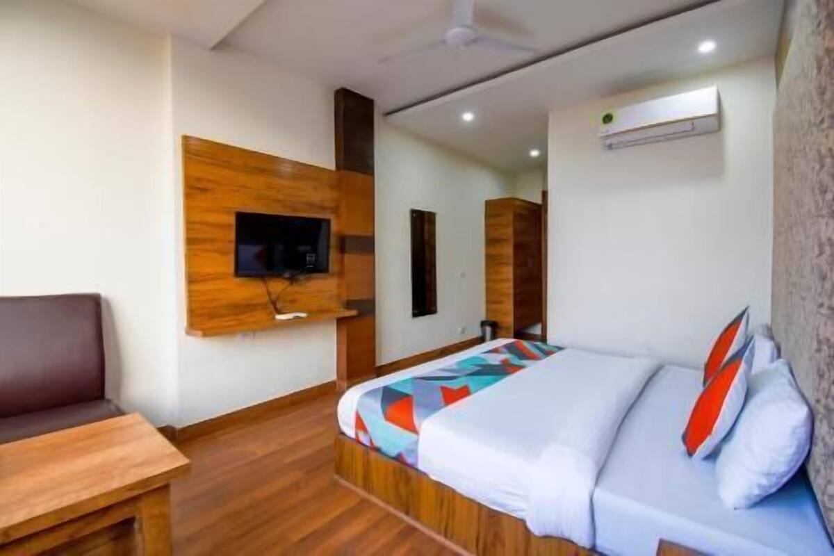 Una habitación de hotel con una cama, un televisor montado en la pared, piso de madera y un ventilador de techo.