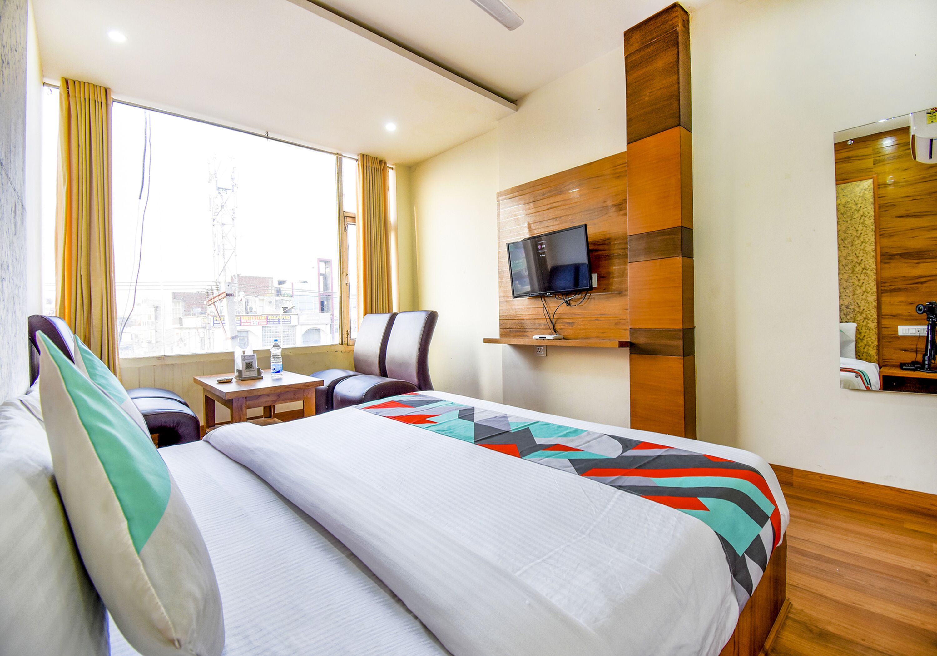 Ein Hotelzimmer mit einem Bett, einem Schreibtisch, einem Sessel, einem an der Wand montierten Fernseher und einem Fenster mit Vorhängen.