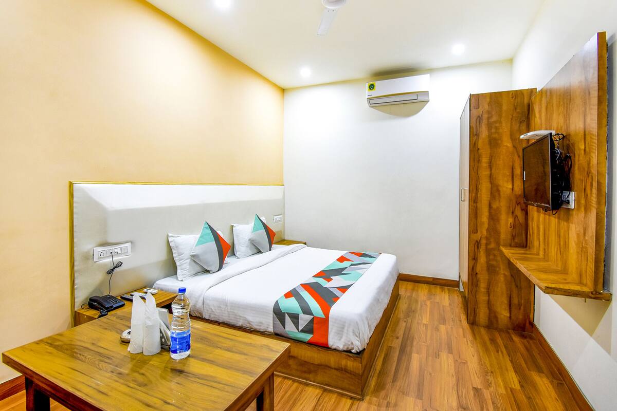 Habitación de hotel con cama, suelo de madera, escritorio con teléfono y botella de agua, y ventilador de techo.