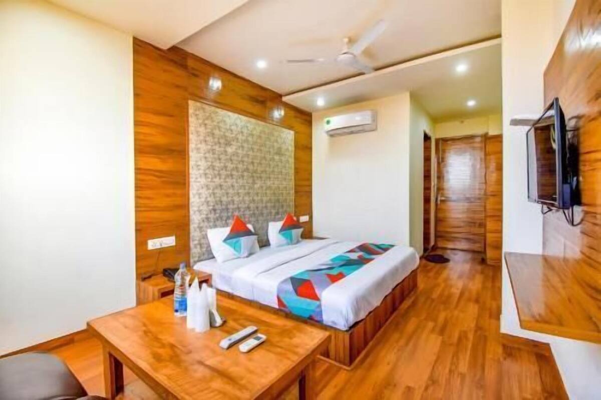 Una habitación de hotel con una cama, suelo de madera, ventilador de techo, aire acondicionado y un televisor montado en la pared.