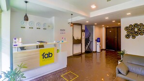 Zona de recepción de un hotel, con mostrador, relojes, una escalera y un sofá.