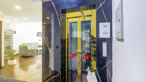 Un ascensor con puerta de vidrio, un cartel que indica la ocupación máxima y un aviso para mantener la distancia y permanecer seguro.