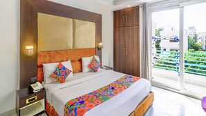 Habitación de hotel con una cama grande, un armario de madera, un teléfono en la mesita de noche y vistas a la ciudad desde la ventana.