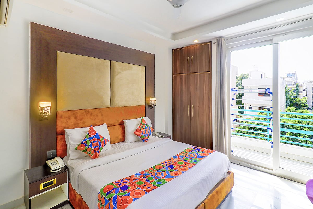 Quarto de hotel com uma cama grande, um guarda-roupa de madeira, telefone ao lado da cama e vista para a cidade pela janela.