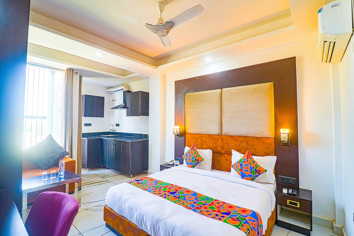 Quarto de hotel com cama, escrivaninha, cadeira, mesa de cabeceira, ar condicionado fixado na parede e ventoinha no teto.