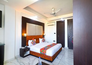 A hotel room with a large bed, a nightstand, a ceiling fan, and a door. - Fabhotel Kiara The Private Suites (Gurugram)