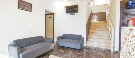 A lobby with two grey sofas, a TV mounted on the wall, a staircase, and a patterned wall decoration.