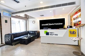Ein Hotel-Empfangsbereich mit modernem Design, der einen Empfangstresen, eine schwarze Ledersofa und einen Flachbildfernseher mit dem Hotelnamen zeigt.