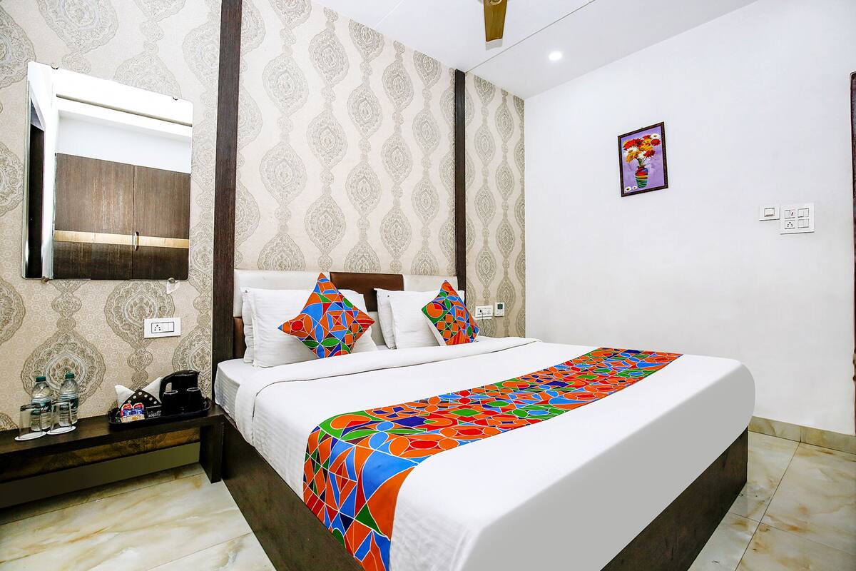 A hotel room with a bed, a bedside table with a lamp, a wall clock, and a painting on the wall.