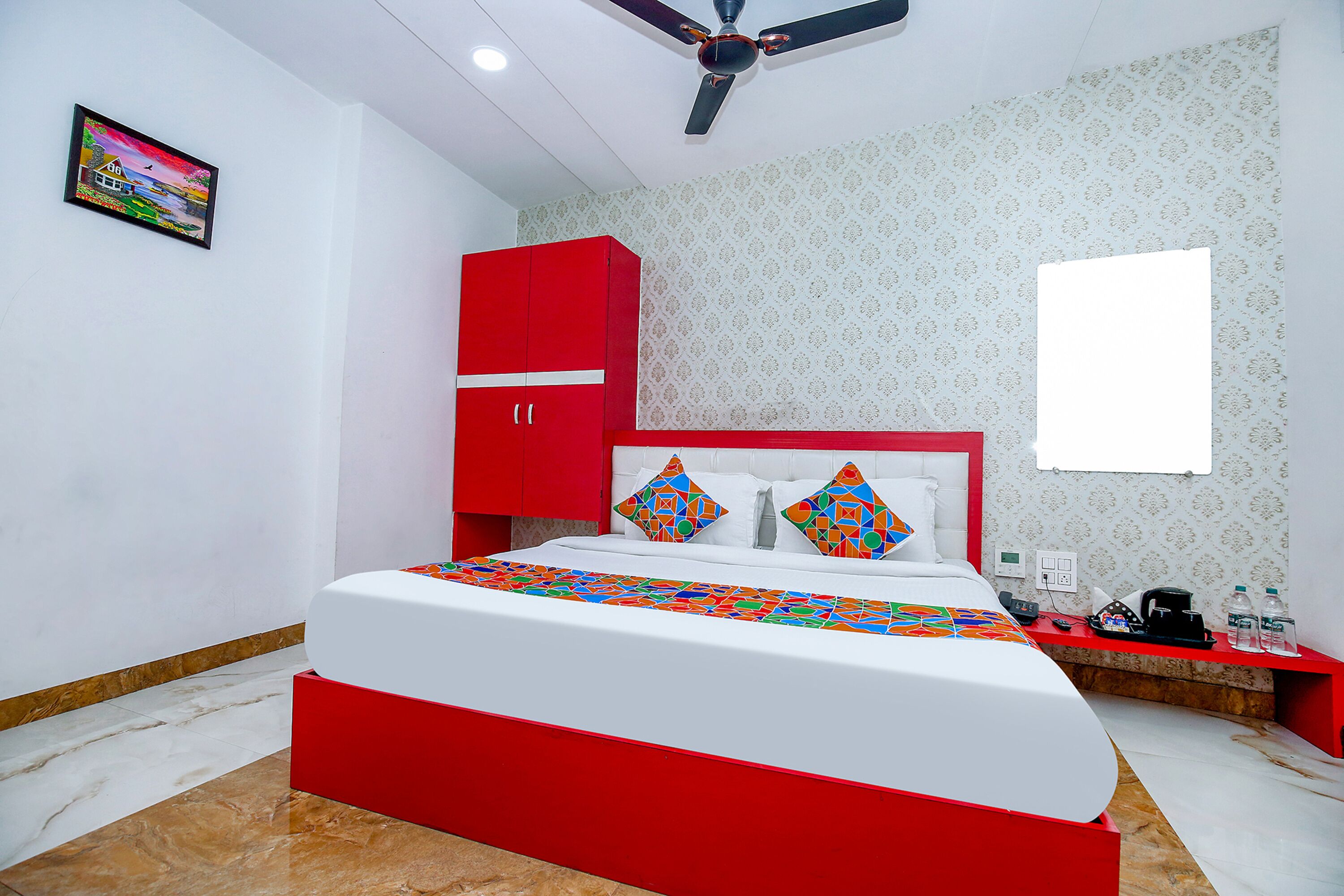 A bedroom with a bed, a red wardrobe, a ceiling fan, and a patterned wall.