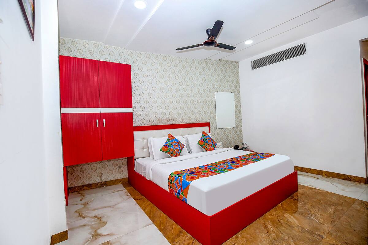 A bedroom with a bed, a red wardrobe, a ceiling fan, and patterned wallpaper.