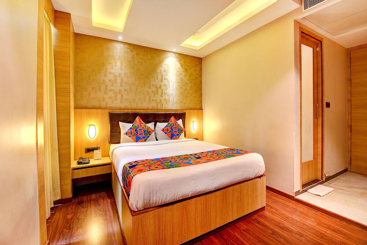 A hotel room with a wooden bed, a nightstand, a wall-mounted light, and a door.