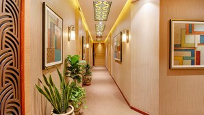 Corredor com obras de arte emolduradas, plantas em vasos e iluminação decorativa.