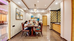 Uma sala de jantar com uma mesa redonda, cadeiras e um lustre. Há também uma cozinha com painel de azulejos e armários de madeira.