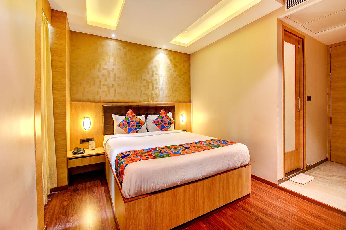 A hotel room with a wooden bed, a nightstand with a phone and a lamp, and a door to the right.