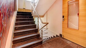Uma escadaria com corrimão, uma porta de madeira com painel de vidro jateado e uma parede com padrão ondulado.