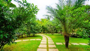 A stone pathway through a lush garden with various green plants and trees. - FabHotel Vagator Retreat Resort With Swimming Pool - Nr. Chapora Fort (Vagator)