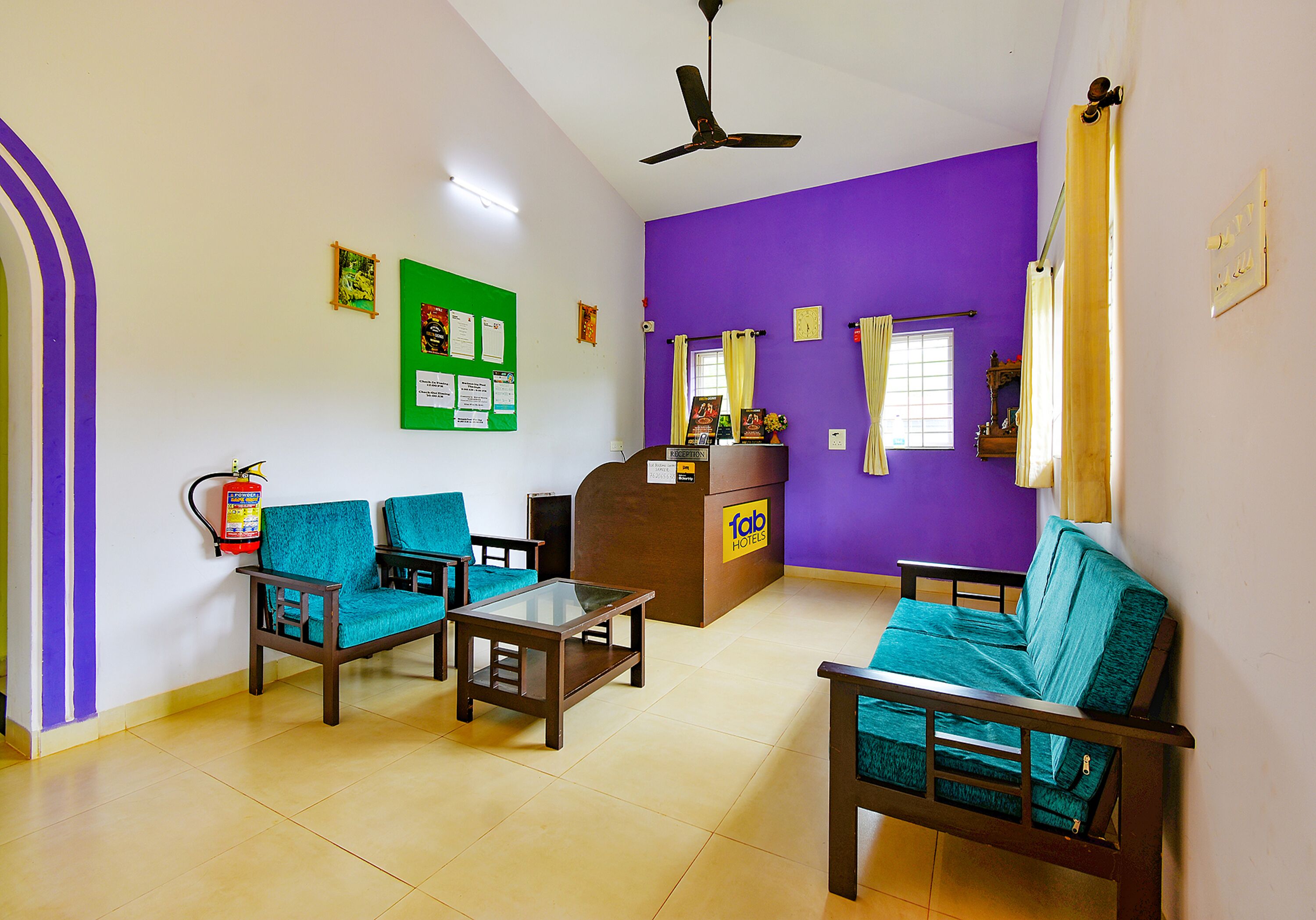 A hotel lobby with teal chairs, a reception desk, and a ceiling fan.