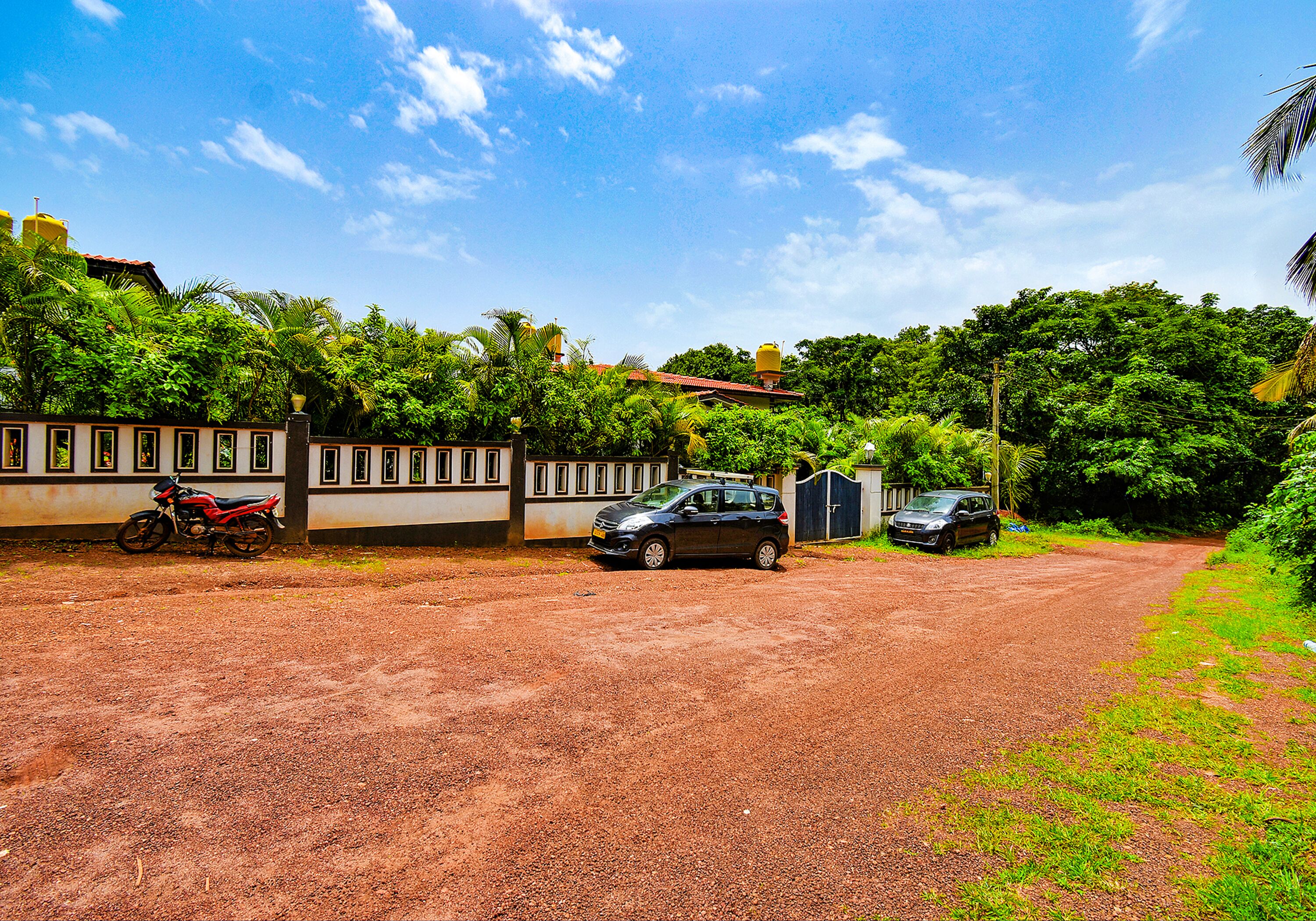 A dirt road leading to a building with a red car parked in front.