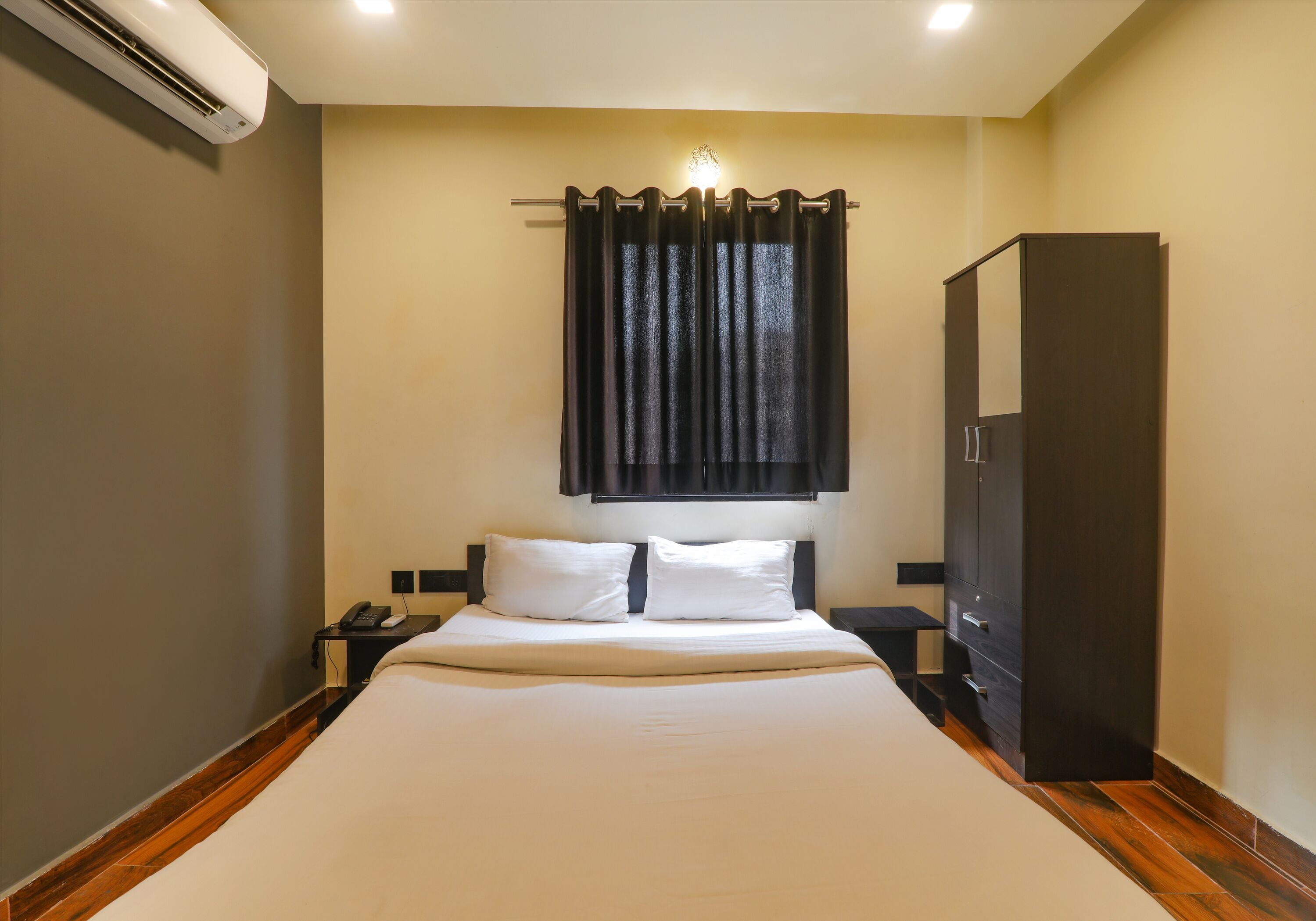 Een hotelkamer met een groot bed, een kledingkast, een nachtkastje met een telefoon en een wandairconditioner.