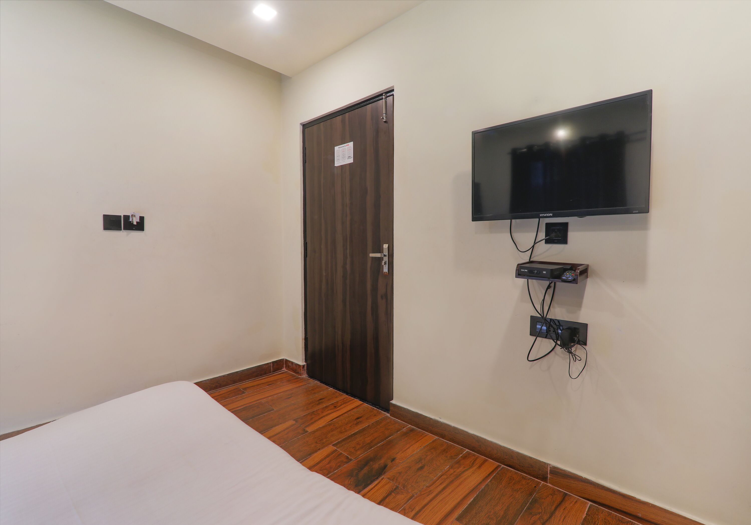 A hotel room with a wooden floor, a bed with white bedding, a wooden wardrobe, and a mounted television.