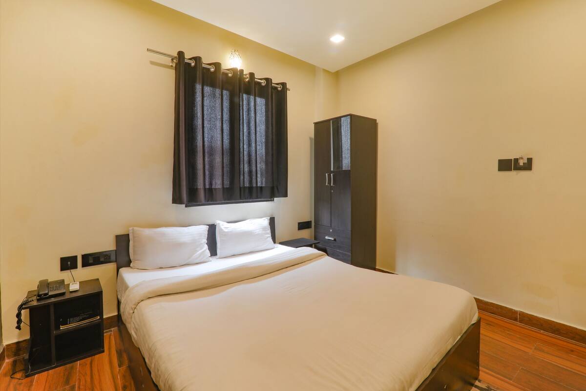 Habitación de hotel con una cama grande, un armario, una mesita de noche con un teléfono y una cortina.