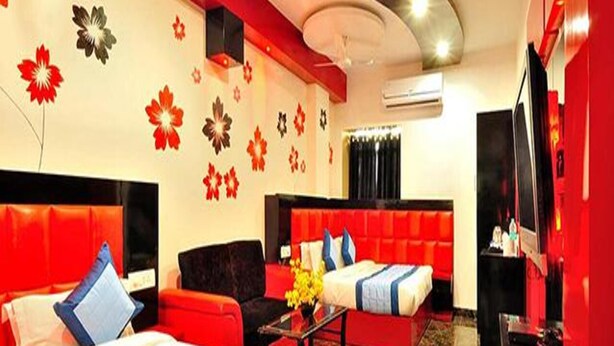 A hotel room with two beds, red upholstered seating, a TV, and decorative wall art. - Fabhotel Arihant Inn (New Delhi)