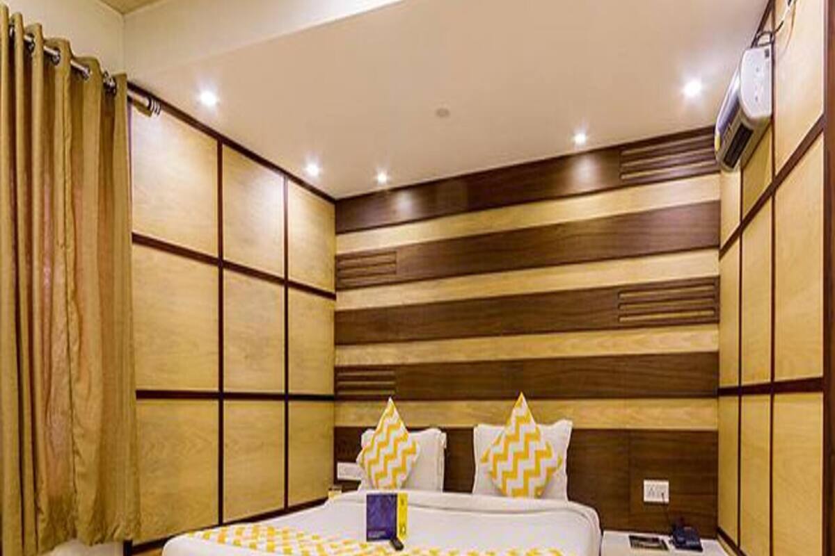 A hotel room with a large bed, wooden panel walls, and a bedside table with a lamp.