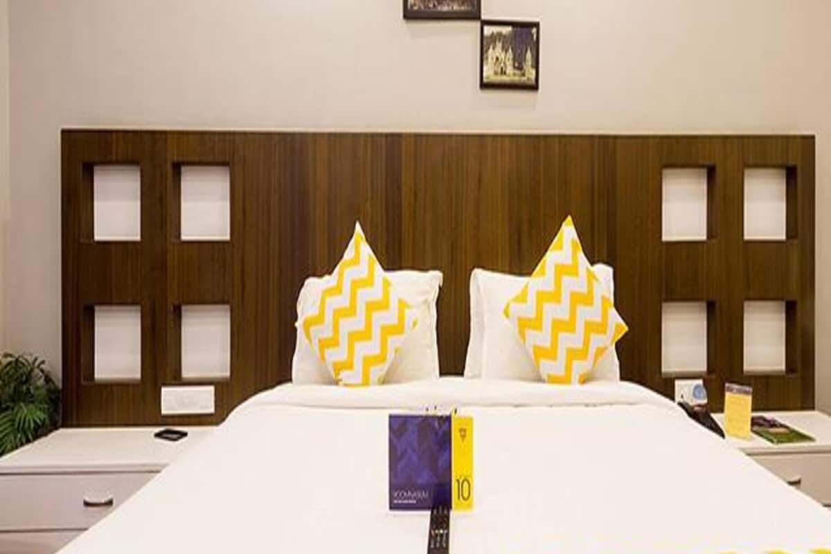 A hotel room with a large bed, wooden headboard with cut-out panels, two pillows with chevron patterns, a remote control, and a book on the bed.