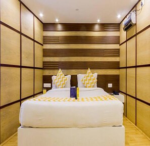 A hotel room with a large bed, wooden panel walls, and a ceiling-mounted air conditioner. - Fabhotel Sholas Residency I (Ootacamund)