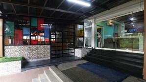 Entrada de hotel con un muro de azulejos, una puerta de cristal y un felpudo azul en los escalones.