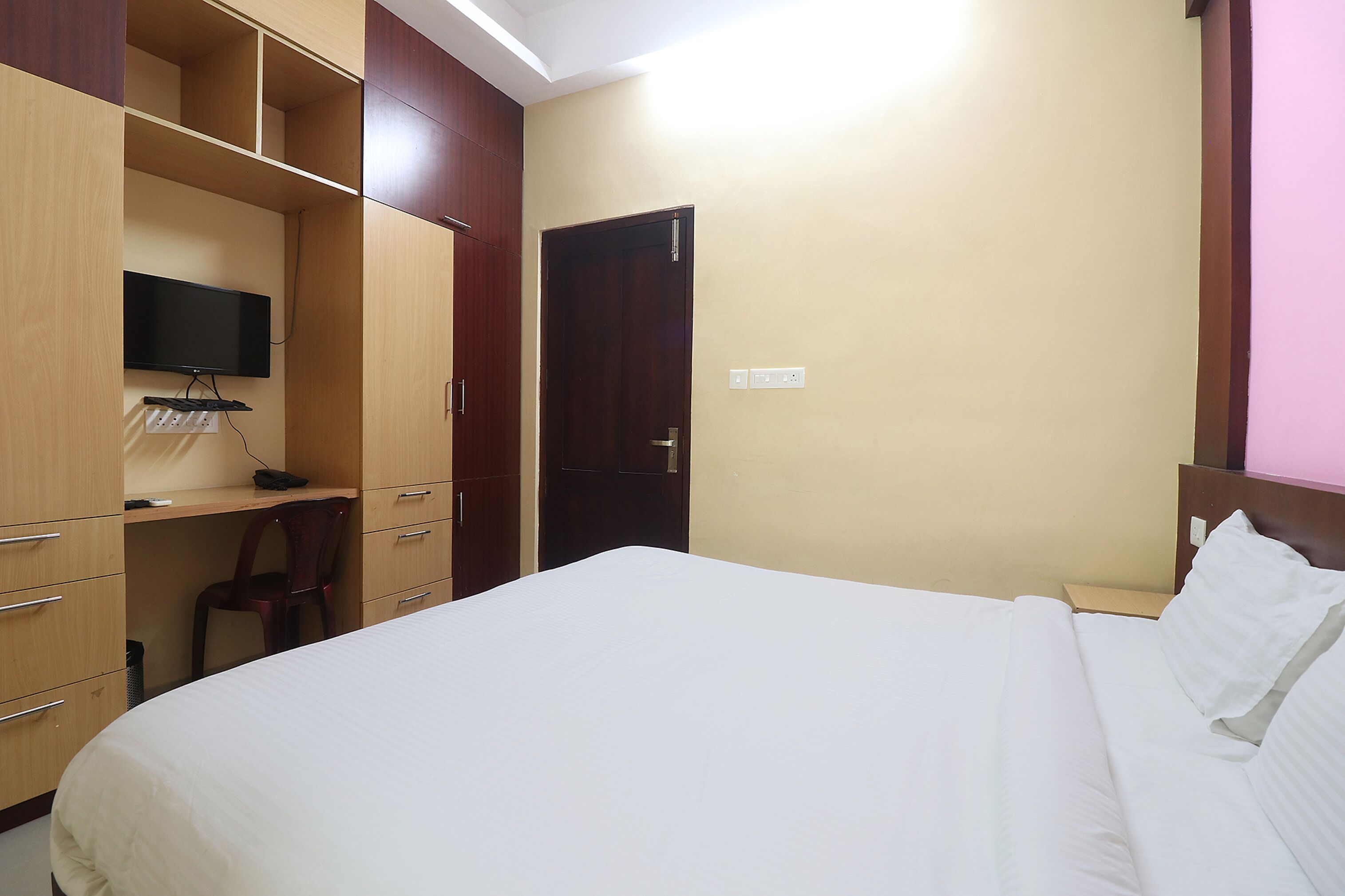 A hotel room with a bed, a desk with a chair, a television, and a wardrobe.