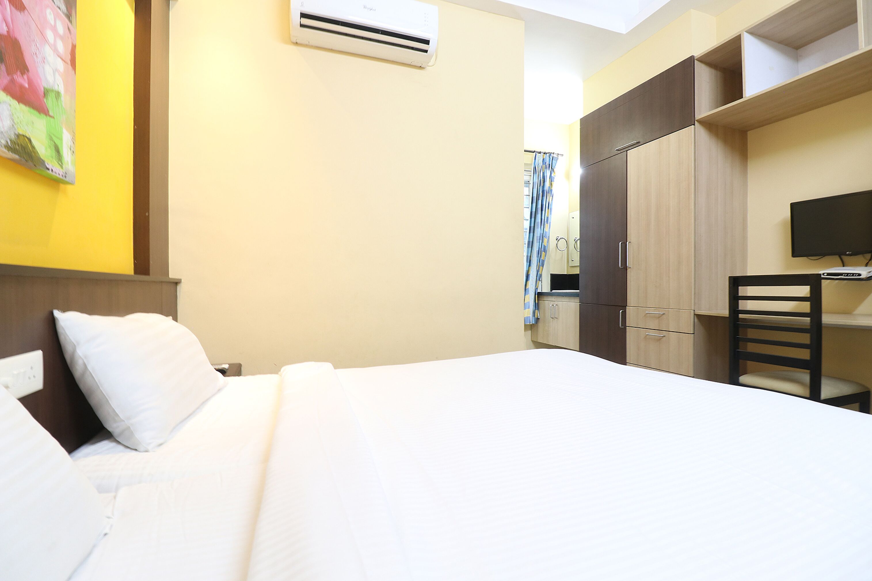 A hotel room with a bed, a desk, a chair, a television, and a wardrobe.