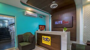Zona de recepción de un hotel, con mostrador de recepción, una escalera que lleva a un piso superior y un cartel que dice 'ELITE Inn'.
