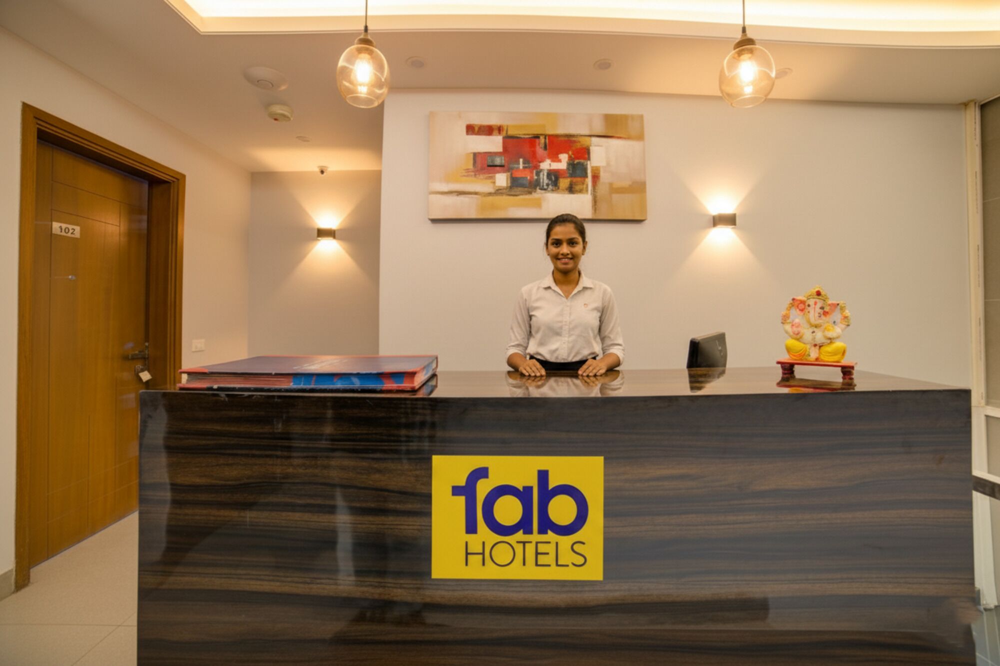 A reception desk at Fab Hotels with a modern design, a framed abstract artwork on the wall, and a small statue on the counter.