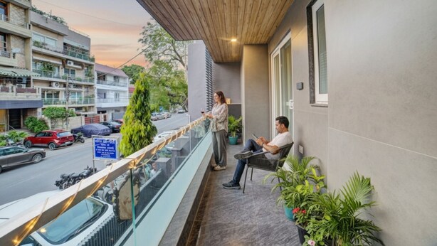 A balcony with a view of a street, a person standing, and another person sitting. - Fabhotel Exotica (New Delhi)