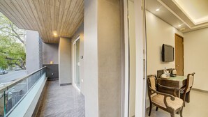 A modern hotel room with a balcony, a dining area with a table and chairs, and a television mounted on the wall. - Fabhotel Exotica (New Delhi)