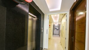 A hotel hallway with elevators, a door, and a corridor leading to another room. - FabHotel Baba Residency (New Delhi)